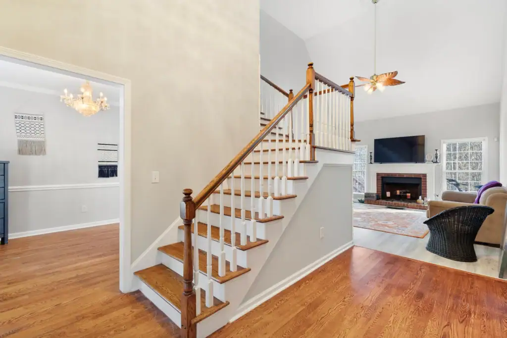 Spacious living room featuring a staircase with wooden handrail, hardwood floors, and a cozy fireplace with a flat-screen TV above.