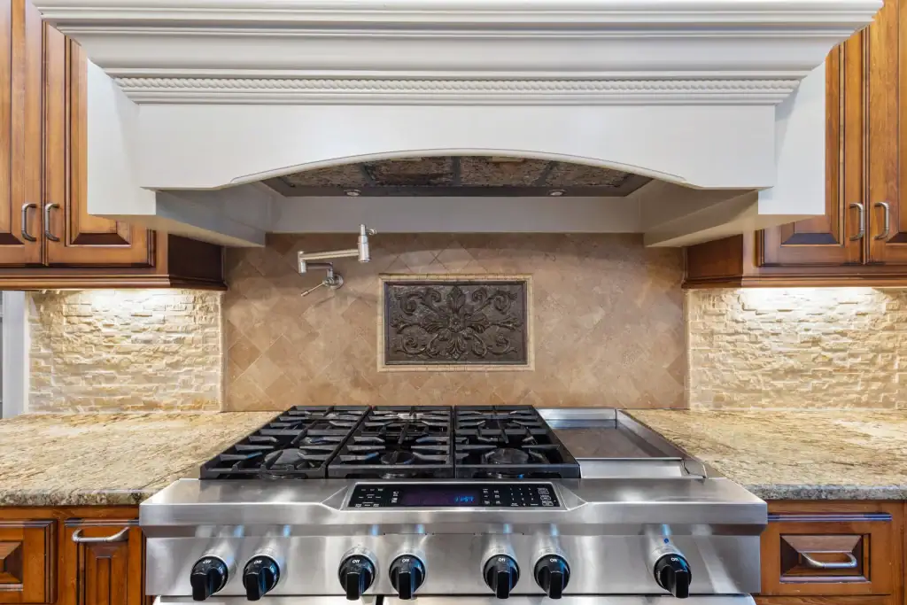 Kitchen stove with stainless steel cooktop and decorative tile backsplash.